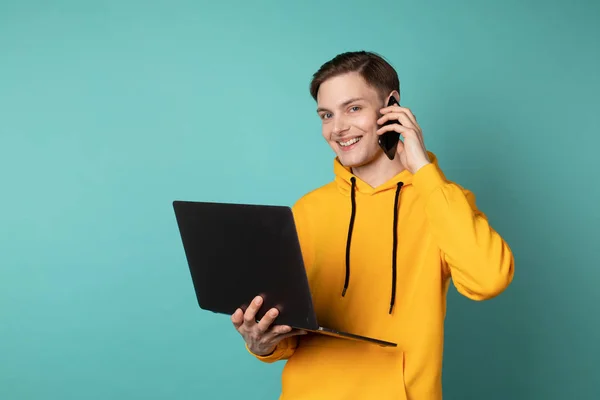 Sarı kapüşonlu genç çekici girişimci dizüstü bilgisayar kullanıyor ve cep telefonuyla konuşuyor.