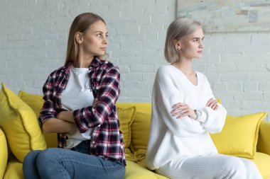 Kavga dan sonra sarı kanepede crosed elleriyle arka arkaya oturan rahat giysiler içinde Lezbiyen kadın çift