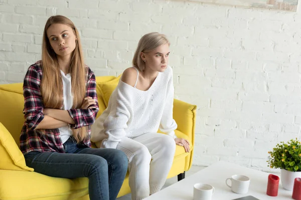 Young offended lesbian couple sitting at home on yellow sofa after quarrel, wearing casual clothes — 스톡 사진