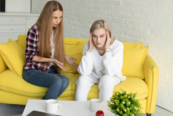 Young lesbian couple in quarrel, wearing casual clothes, sitting on yellow sofa at home — 스톡 사진