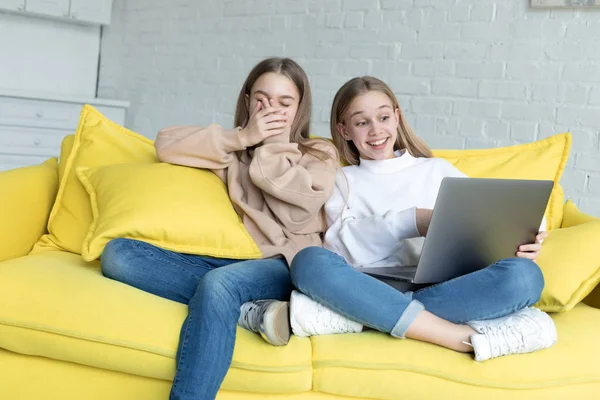 Två unga honor vänner tittar tillsammans rolig film på laptop medan du sitter tillsammans på soffan hemma — Stockfoto