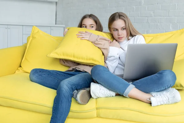 Två små flickor i casual kläder sitter tillsammans på gula soffan hemma — Stockfoto