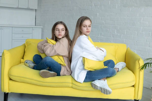 Hermanas jóvenes con ropa casual sentadas en un sofá amarillo espalda con espalda después de la pelea —  Fotos de Stock