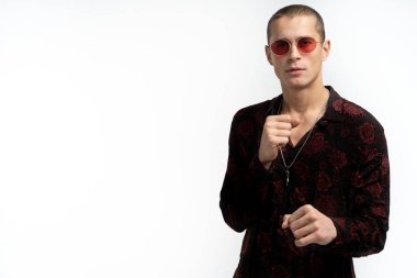 Kırmızı güneş gözlüğü ile gül baskılı trendy şık siyah gömlek Çekici genç adam önünde yumruktutar eğer onu, kameraya bakarak, beyaz arka plan üzerinde izole