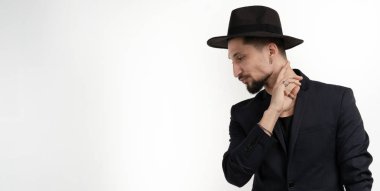 Siyah trendy takım elbise ve şapka ile şık sakallı genç adam yüz yakın el tutarak, beyaz arka plan üzerinde izole sol aşağı bakıyor, metin için copyspace