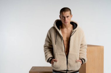 Kısa saç kesimi ile emin ciddi yakışıklı adam, şık spor giyim giyiyor, kameraya bakıyor, ceplerinde el ele tutuşarak, beyaz arka plan üzerinde izole, metin için copyspace