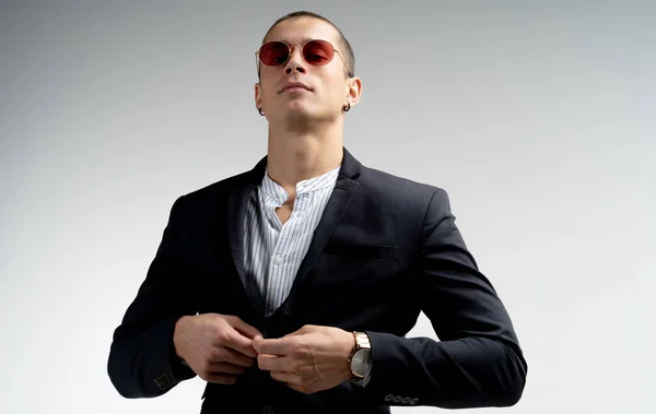 Элегантный уверенный молодой бизнесмен с короткой стрижкой в красных солнцезащитных очках в черном костюме на белом фоне — стоковое фото