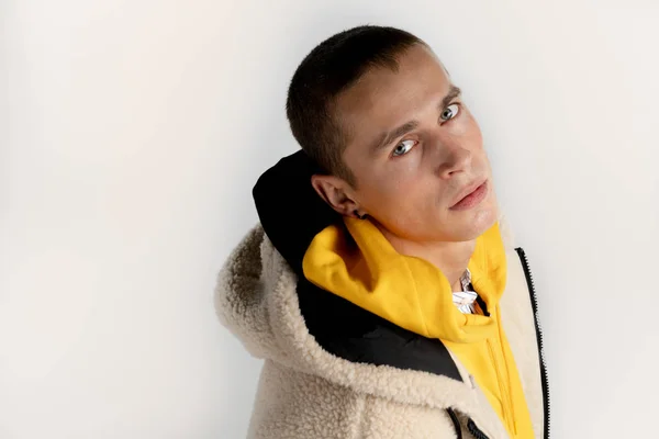 Porträt eines ernsthaften attraktiven jungen Mannes in gelbem Kapuzenpulli, der isoliert vor weißem Hintergrund in die Kamera blickt — Stockfoto