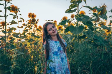 Çiçekleri ile elbise güzel esmer genç kız gülümseyerek ve kameraya bakarak ayçiçekleri arasında duran baskı