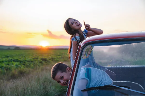 Petite sœur et frère heureux sont sortis par la fenêtre de la voiture et s'amuser pendant le voyage en voiture, coucher de soleil sur le fond — Photo