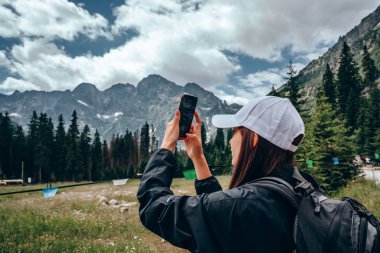 Siyah ceket sırt çantası ile kadın gezgin dağların güzel bir panorama bir telefon fotoğrafı yapar