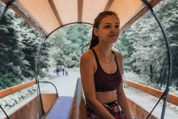 Atractiva joven morena cabalga en un vagón entre el bosque y las montañas, mirando con calma —  Fotos de Stock