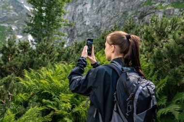 Sırt çantası ile siyah ceket genç esmer kız gezgin dağlarda telefon fotoğrafı yapma, aktif yaşam tarzı kavramı