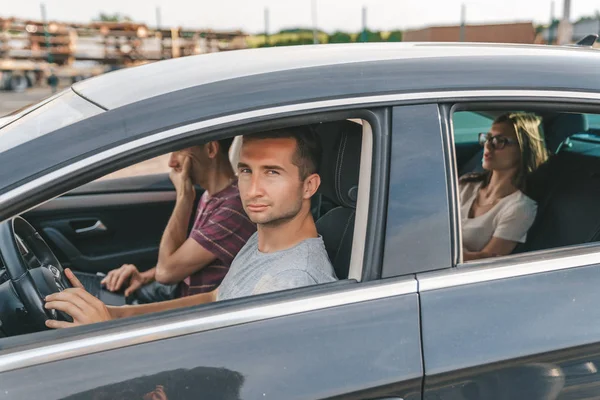 Young attractive man in grey t-shirt driving a car with friends