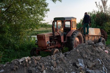 Ukrayna, Chernivtsi, 10 08 2019 Göl kenarında tank ile eski kırmızı traktör, iş kıyafetleri adam çiftçi varil püskürtücü ayakta