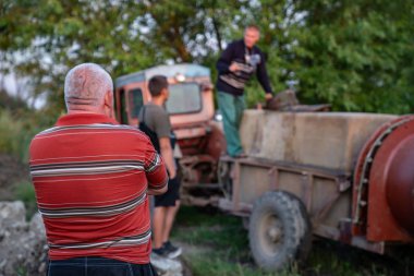 Ukrayna, Chernivtsi, 10 08 2019 Man patron çiftçi veya bahçıvan çapraz elleri ile kameraya geri duran ve çalışanları bir traktör arıza ile sorunu çözmek nasıl bakıyor