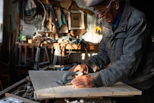 Gri giysi ve gözlük evde çalışan eski kıdemli marangoz, ahşap parlatır — Stok fotoğraf