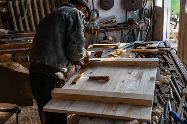 Senior-Schreiner in grauer Kleidung, der Holzarbeiten in der heimischen Werkstatt macht, konzentriert sich auf die Arbeit — Stockfoto