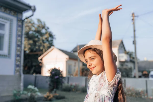 Retrato de vista lateral de niña linda en sombrero y vestido con las manos levantadas, foto al aire libre — Foto de Stock