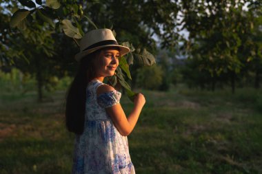 Beyaz şapkalı İspanyol kızın yan görünüm portresi ve bahçede yaz tatilinin tadını çıkarak uzağa bakan elbise