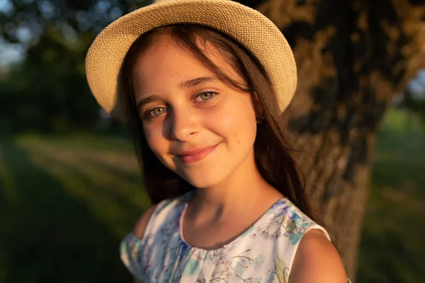 Gros plan portrait de jeune belle fille avec une peau naturelle saine portant chapeau blanc souriant et regardant la caméra, grand arbre sur le fond — Photo