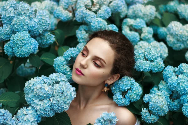 Joyeux tendre jeune fille avec une peau naturelle saine et lèvres rouges debout parmi les fleurs bleues avec des épaules nues — Photo