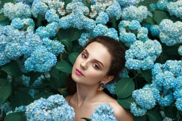 Chica joven alegre y tierna con la piel natural sana y labios rojos de pie entre flores azules con hombros desnudos — Foto de Stock