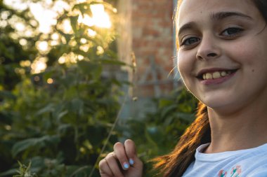 Doğal sağlıklı cilt ve diş ile genç kız yakın portre bu gülümseyerek ve kameraya bakarak, arka planda gün batımı