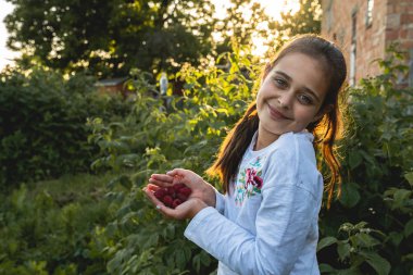 Mutlu gülümseyen esmer kız o arka bahçesinde toplanan avuç içi ahududu gösteren, yaz tatili