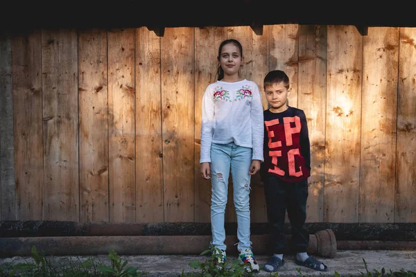 Niño y niña en ropa casual de pie seriamente juntos aislados sobre fondo de madera, mirando hacia otro lado — Foto de Stock