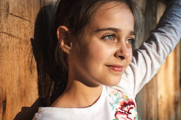 Portrait extérieur en gros plan d'une étonnante petite fille brune avec une peau naturelle et saine regardant sérieusement ailleurs, isolée sur un fond en bois — Photo