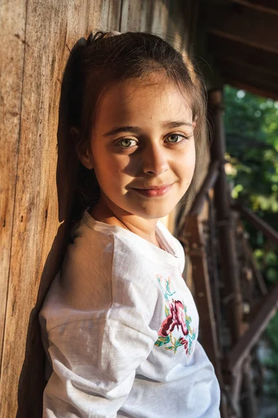 Portrait à mi-longueur d'une jolie jeune fille brune aux yeux verts qui s'appuyait sur un mur en bois et regardait la caméra avec un sourire — Photo