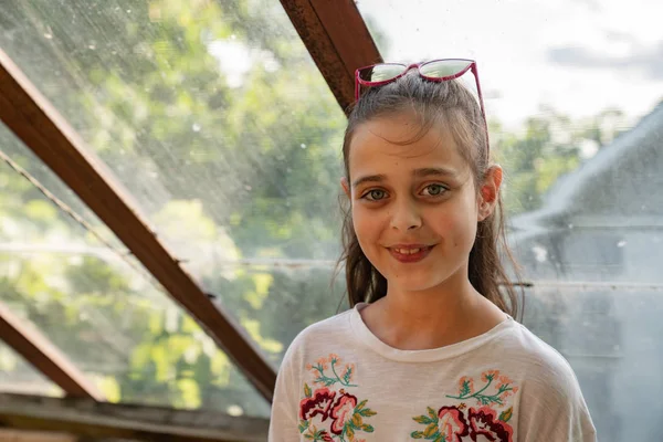 Petite fille attirante en t-shirt blanc avec des lunettes de soleil roses sur la tête en regardant la caméra, les fenêtres du toit sur le fond — Photo