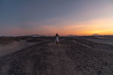 İnanılmaz panorama, çöl arasında duran beyaz elbiseli güzel esmer kız, arka planda renkli gökyüzü