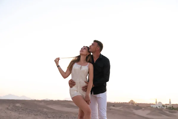 Pareja romántica joven en ropa elegante de pie entre el desierto abrazando y mirando a la esquina superior izquierda — Foto de Stock