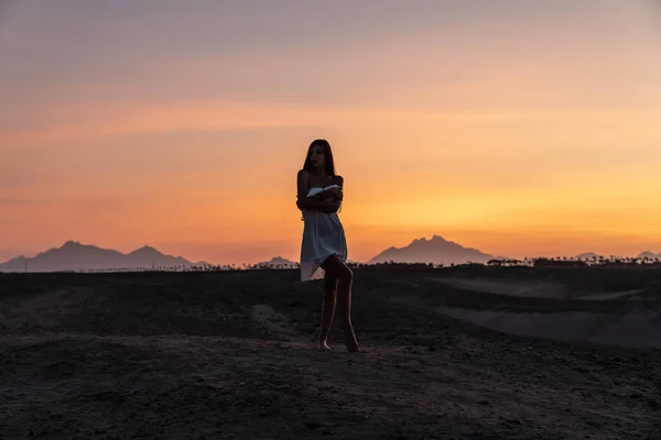 素晴らしいパノラマ、砂漠の間に立つ白いドレスで美しいブルネットの女の子、背景にカラフルな空 — ストック写真