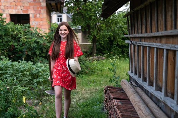 Hermosa chica con la cabeza roja en vestido caminando entre el jardín con pala en las manos, vacaciones de verano en el pueblo — Foto de Stock