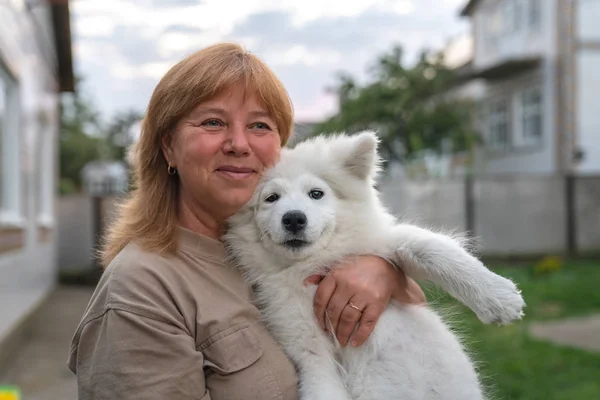 Close up ritratto di felice donna bionda sorridente che tiene cucciolo samoyed bianco sulle mani — Foto Stock