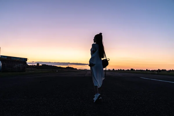 Chica joven con el pelo largo de pie de nuevo a la cámara y mirando a la distancia, puesta de sol en el fondo — Foto de Stock