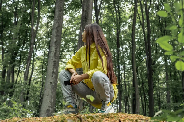 Jeune fille aux cheveux longs assise sur un tronc d'arbre dans la forêt printanière. Femme randonneuse au repos — Photo