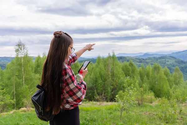 Una giovane donna in piedi di nuovo alla macchina fotografica sulla cima di una collina, controllando qualcosa nel suo telefono e indicando qualcosa in lontananza Fotografia Stock
