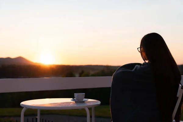 Frau allein auf der Terrasse und beobachtet den Sonnenuntergang über den Bergen im Sommerurlaub Stockfoto