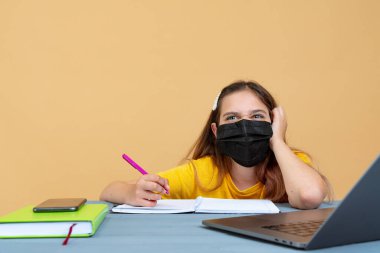 Uzaktan öğrenme çevrimiçi eğitim. Tıp maskeli kız evde çalışıyor, dizüstü bilgisayar başında çalışıyor ve okul ödevlerini yapıyor.