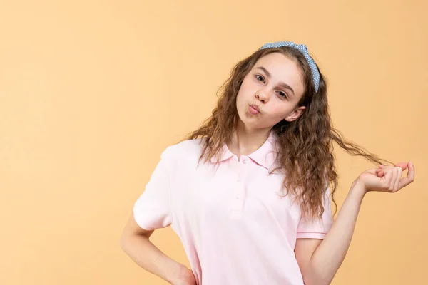 Muchacha adolescente atractiva tocando su pelo rizado mirando a la cámara, enviando beso de aire, retrato de estudio —  Fotos de Stock