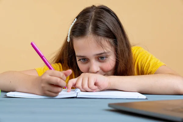 Estudiante universitaria o escolar adolescente hispana escribiendo en un libro de trabajo haciendo la tarea o preparándose para el examen sentado en el escritorio — Foto de Stock