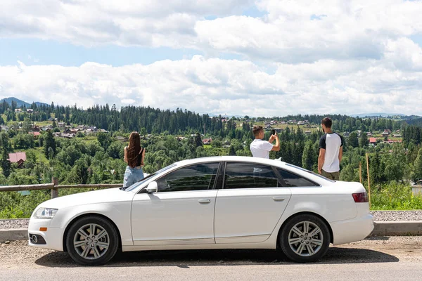 Freie Fahrt mit dem Auto. Auto mit drei Freunden oben auf dem Hügel mit schöner Aussicht auf die Berge — Stockfoto