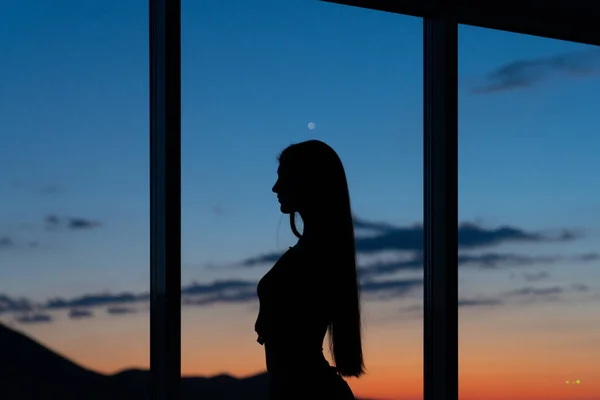 Silhueta de mulher ao sol na janela com vista para o pôr do sol nas montanhas — Fotografia de Stock