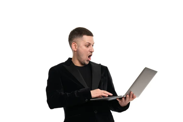 A shocked man holds a laptop in his hands and looks at him with surprise with his mouth open and big eyes. Isolated — Stock Photo, Image