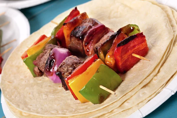 Piknik masasında biftek ve sebzeli barbekü şişi.