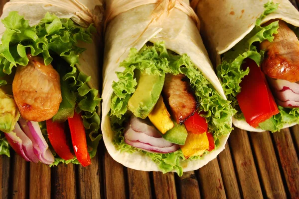 Marinated chicken with avocado wrap sandwiches on wooden woven mat